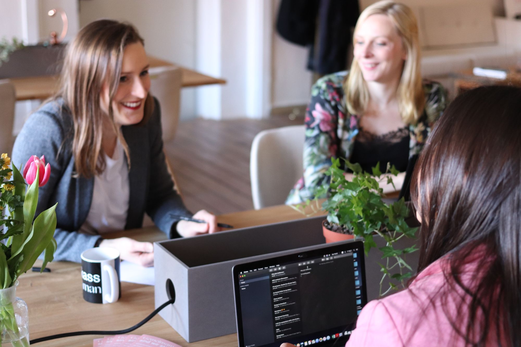 Three women talking together around a table in a bright office