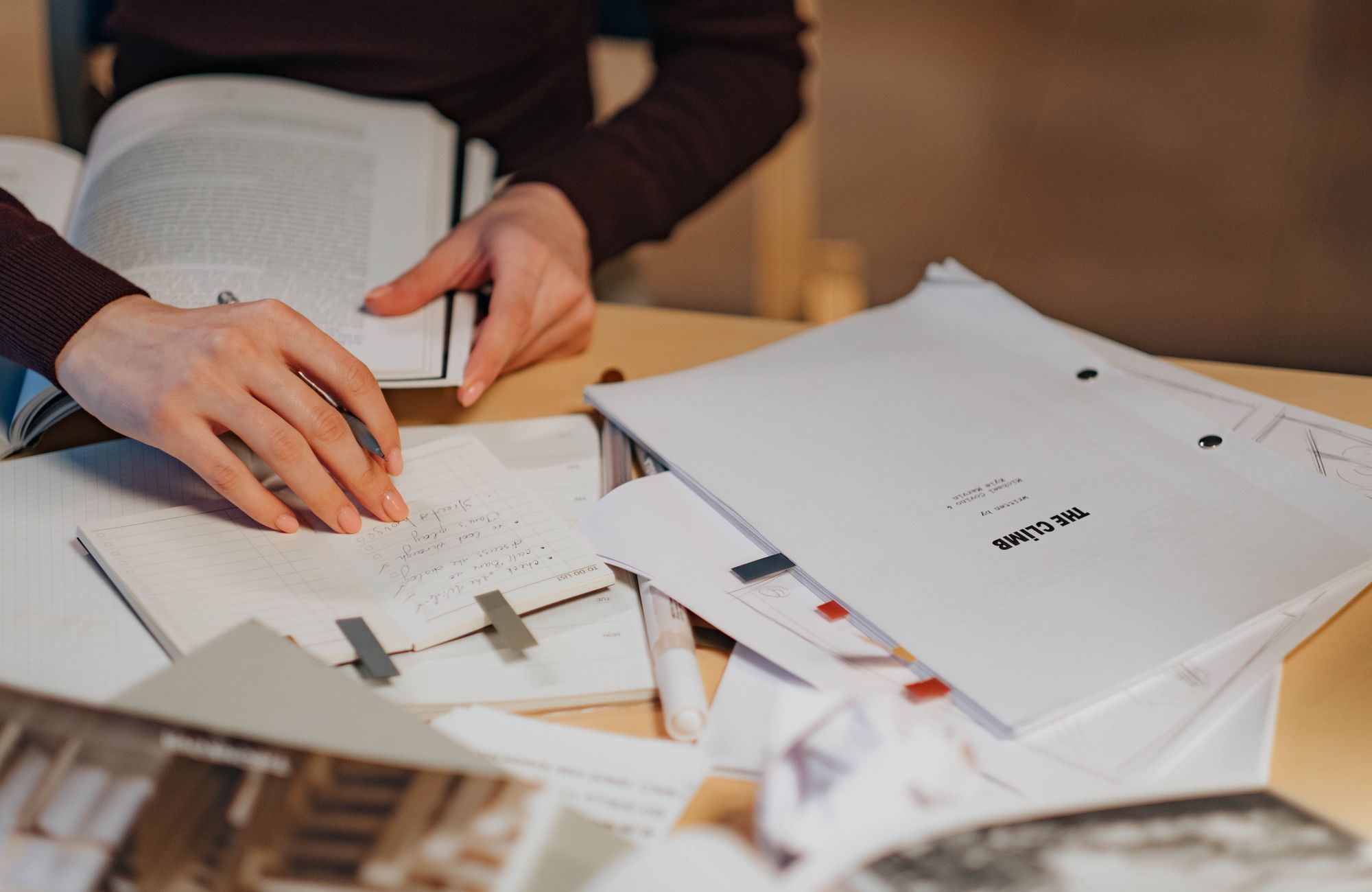 A woman's hands writing notes beside papers and an open book