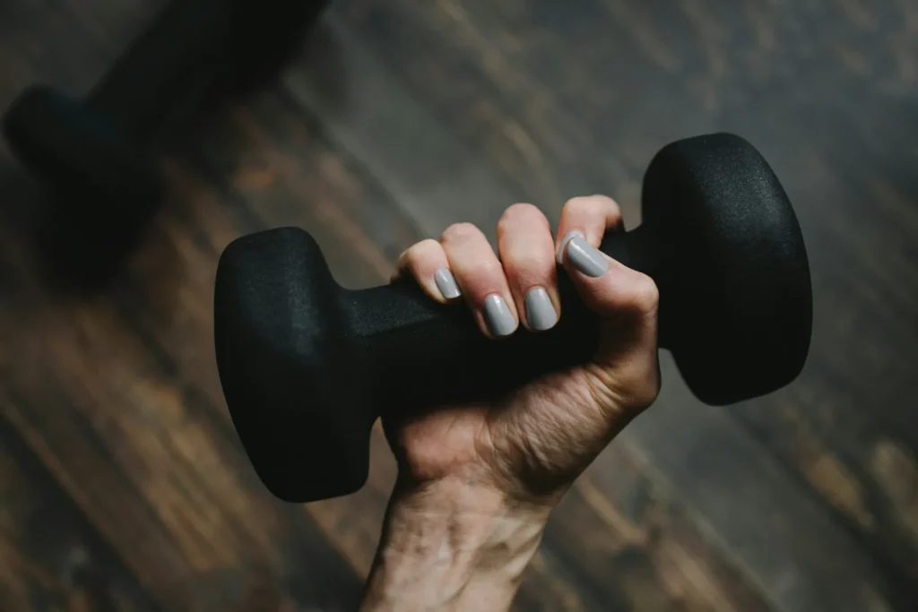 A woman's hand gripping a black dumbbell above a wooden floor