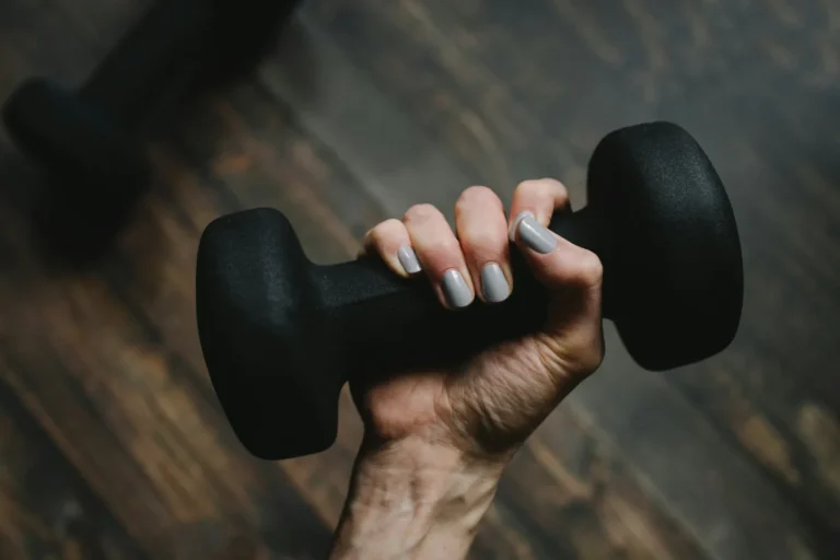 A woman's hand gripping a black dumbbell above a wooden floor