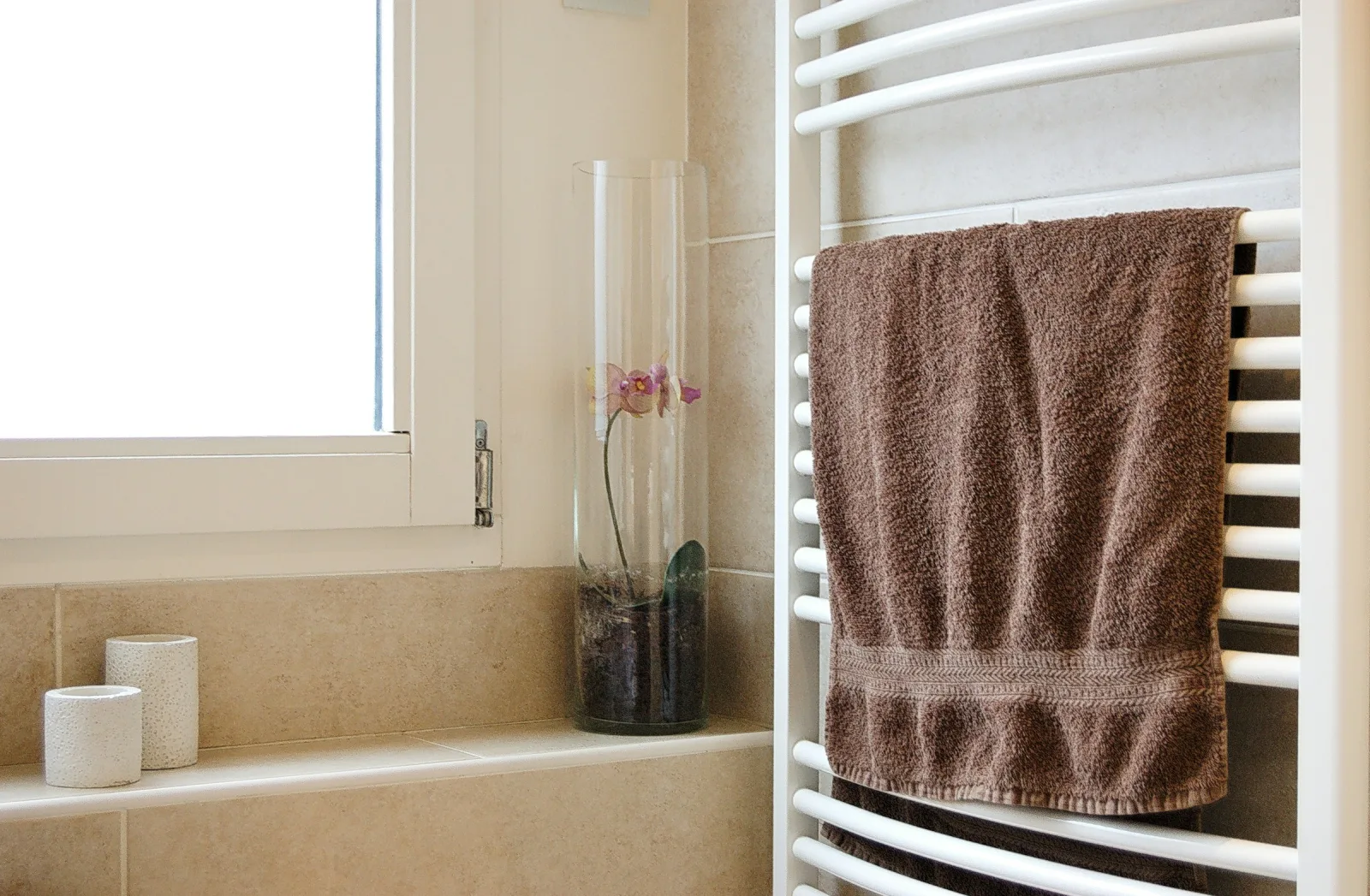 A towel hanging on a white heated towel rail beside a bathroom window, a calm space for a daily routine