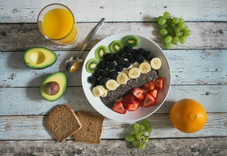 A bowl topped with chia seeds, blackberries, strawberries, kiwi and banana, next to whole-grain bread, avocado, grapes and an orange