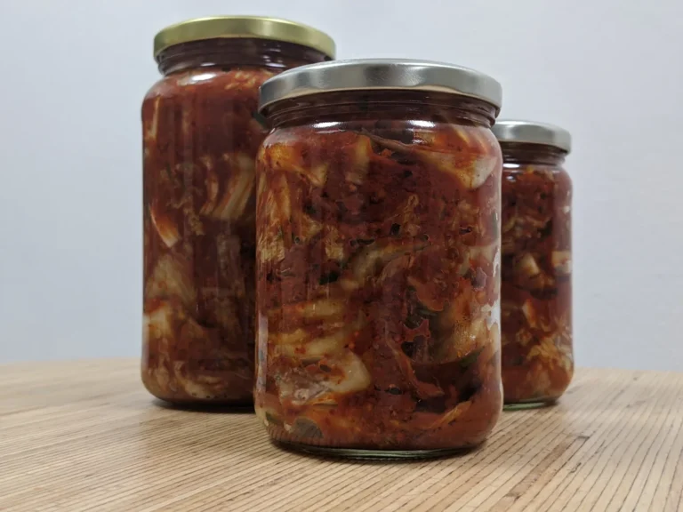 Three glass jars of homemade kimchi, a fermented cabbage dish, on a wooden table