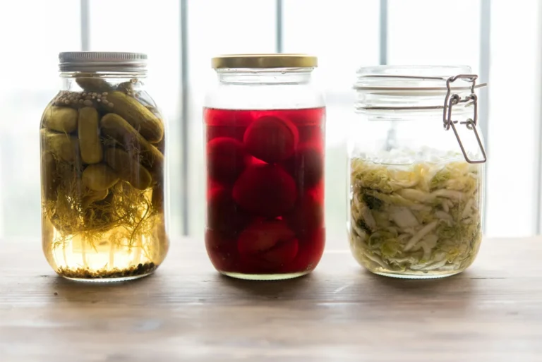 Three glass jars of homemade fermented vegetables, pickled cucumbers, beets and sauerkraut, on a table by a bright window