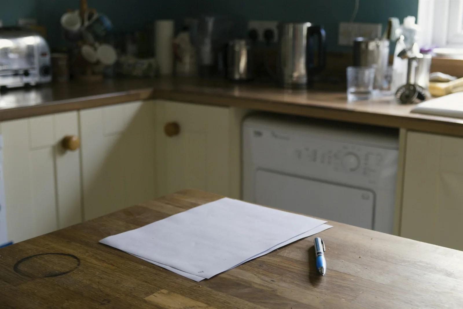 A sheet of paper and a pen on a wooden kitchen table, ready for writing down questions