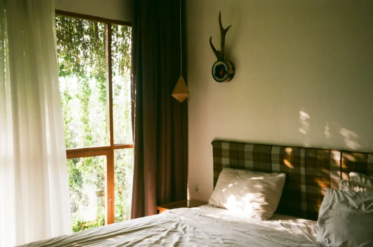 A quiet bedroom with a neatly made bed and soft daylight coming through a large window
