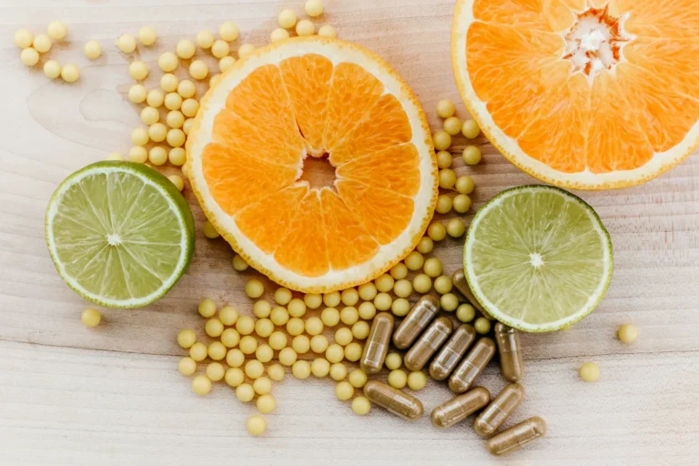 Supplement capsules and small round softgels scattered beside halved oranges and limes on a light wooden table